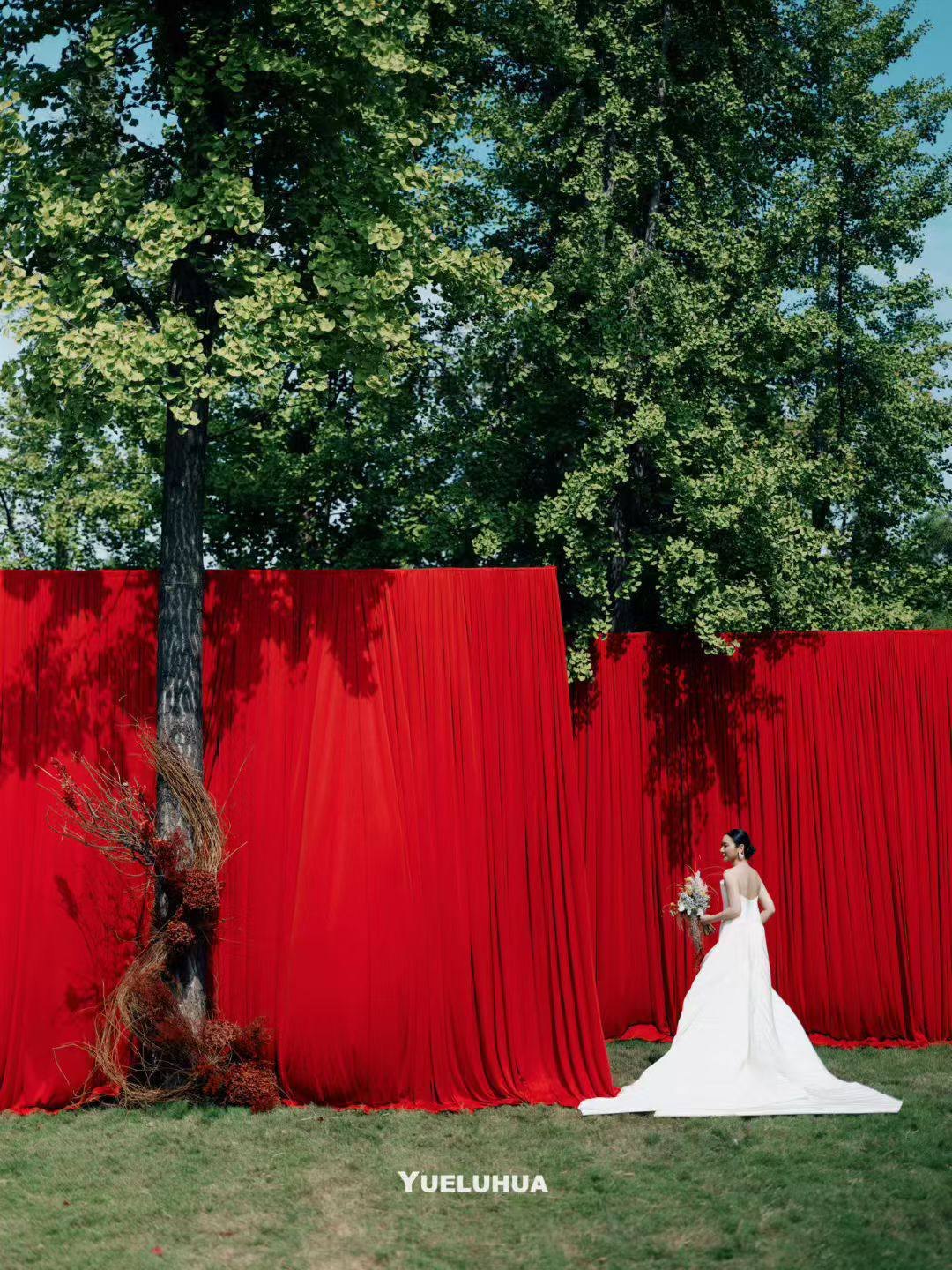 The bride against vivid red drapery beneath green trees