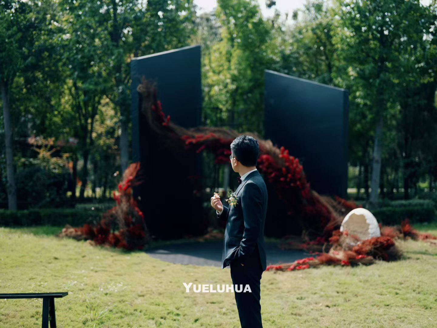 The groom beside the sweeping red floral composition