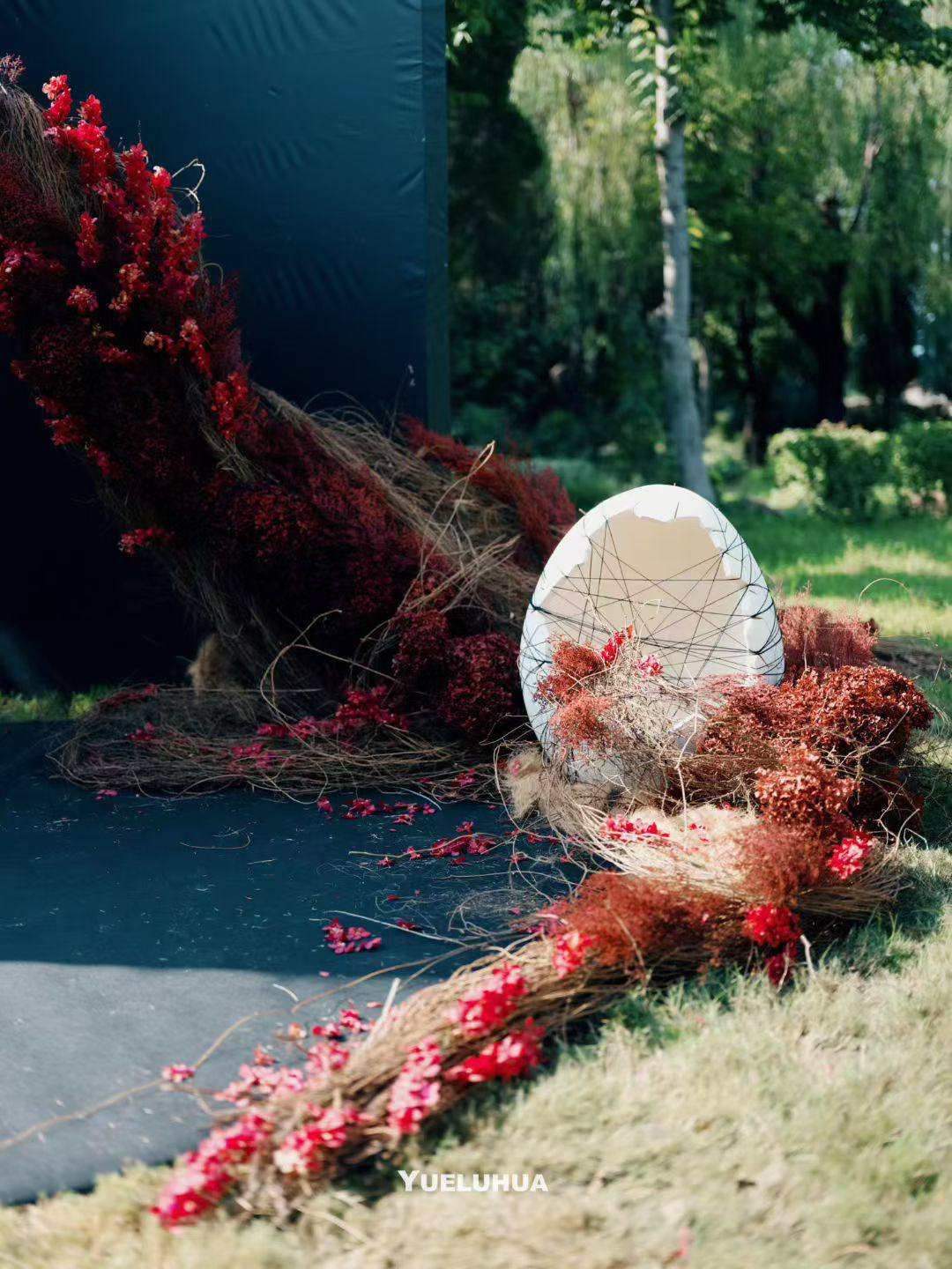 A woven form and crimson flowers beside the ceremony aisle