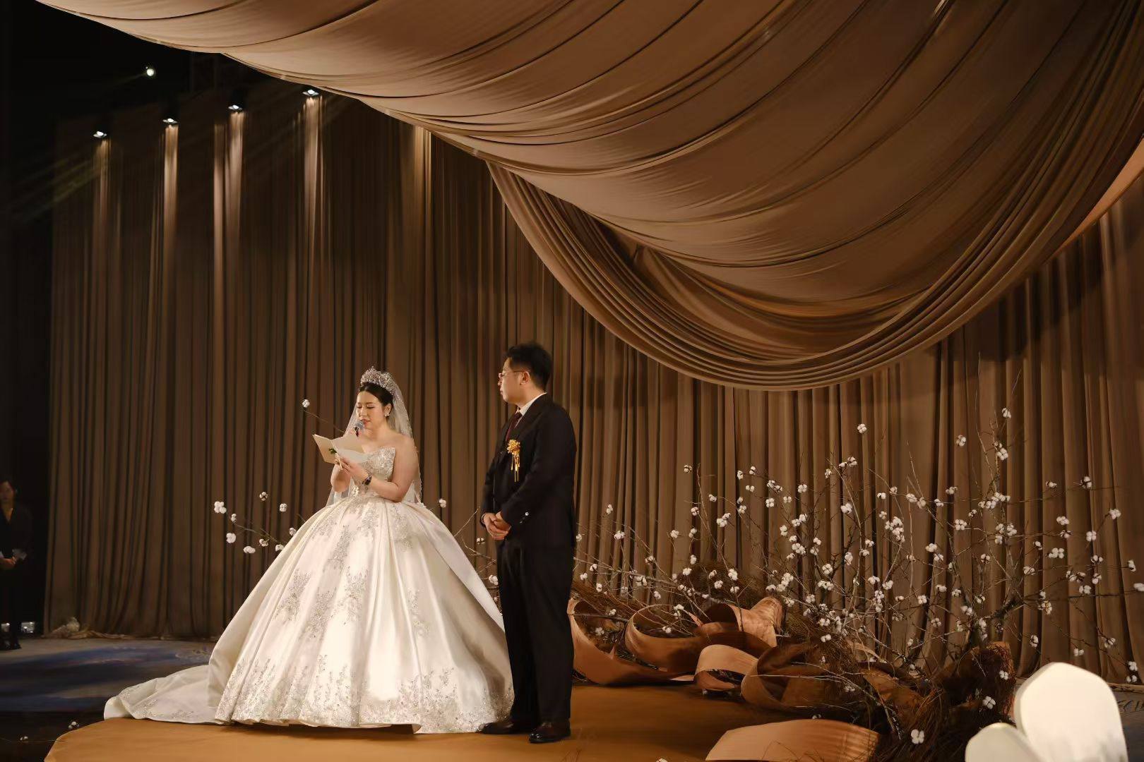 The couple on a stage beneath warm gathered fabric