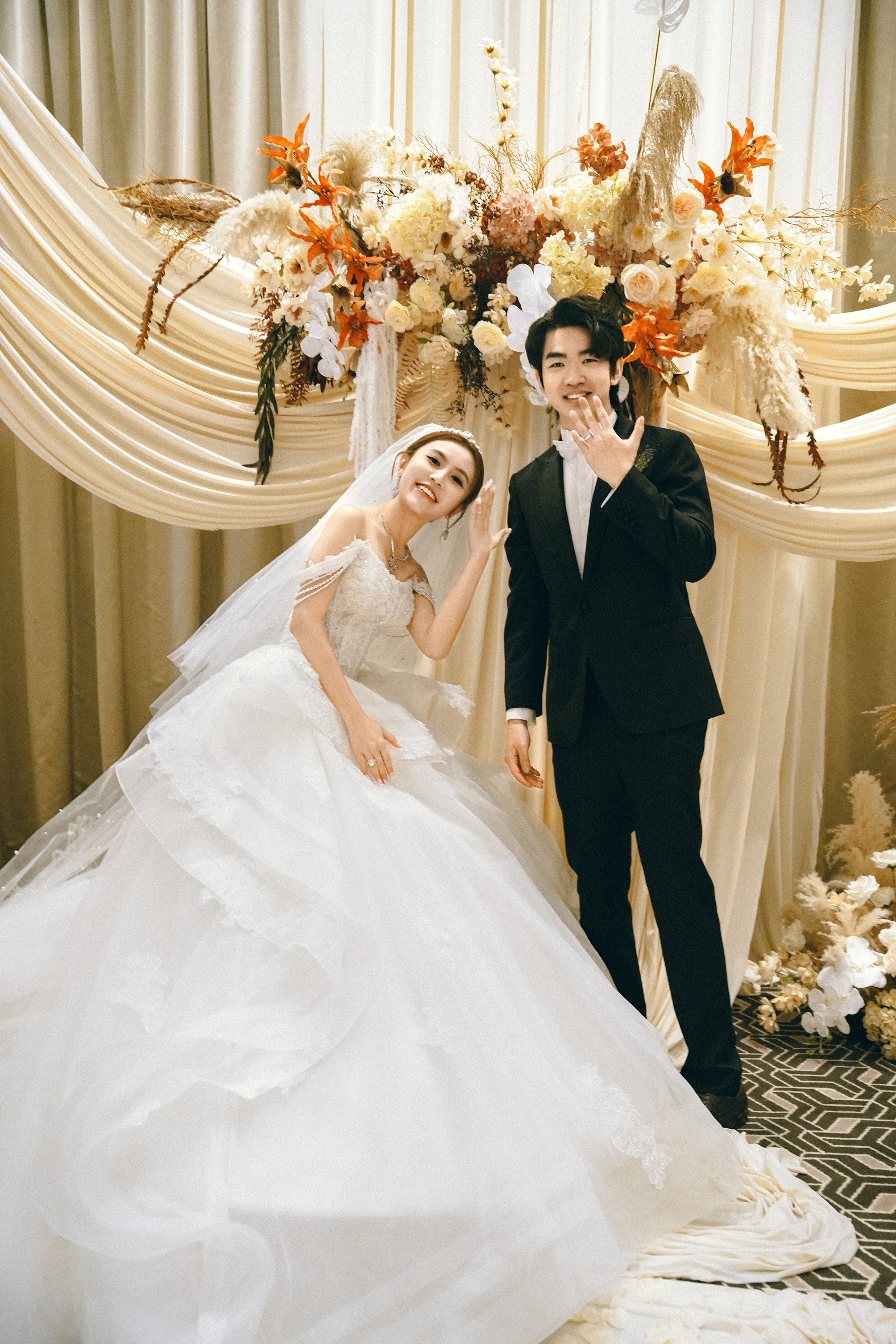 The couple celebrating in front of warm flowers and gathered ivory fabric