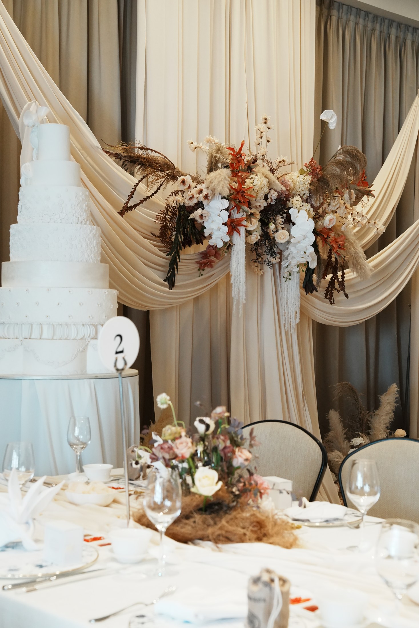 Gathered ivory fabric and warm floral arrangements beside a wedding cake